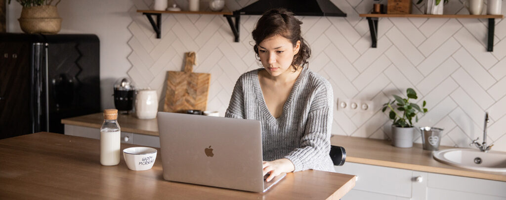 Woman in kitchen looking at her Apple Macbook