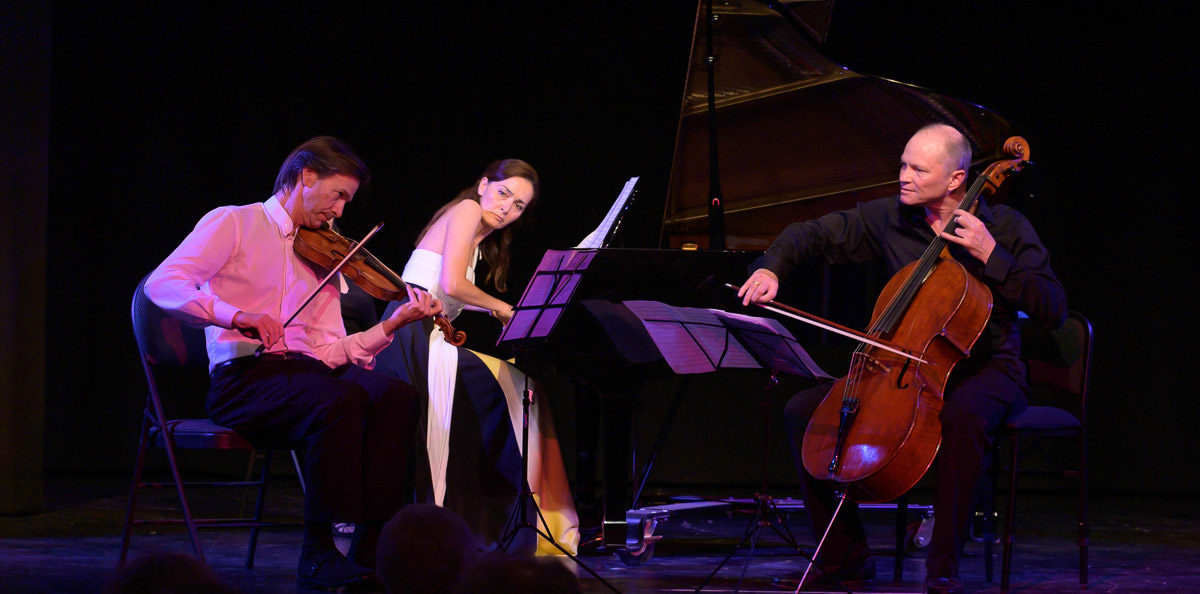 Violinist, pianist and cellist performing on dark stage